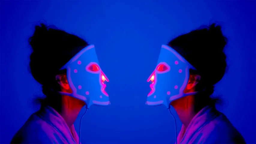 Two women in LED masks sitting facing each other