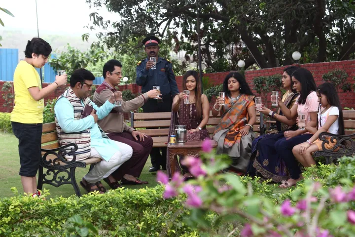 Why is everyone in Sai Dham Society carrying a glass of water?