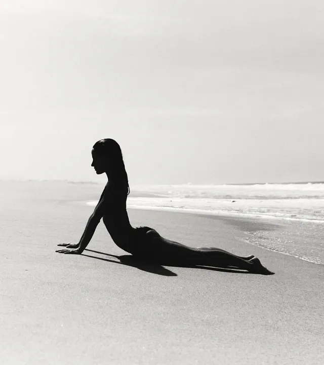 A woman practising the Bhujangasana yoga pose by the beach