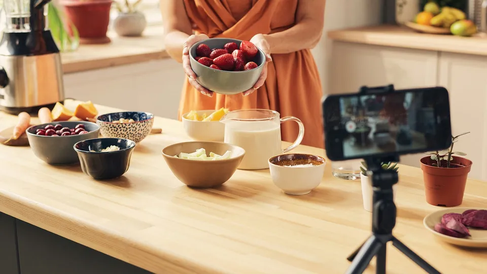 A woman recording a food preparation video with fresh ingredients on a kitchen counter, showcasing cooking as a hobby and content creation in India