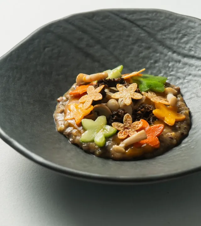 A picture of star-shaped colourful pieces on top of a dish served in a fancy, black, deep bowl to show how vegetarian fine dining in India and vegetarian tasting menus India are having such a large impact.
