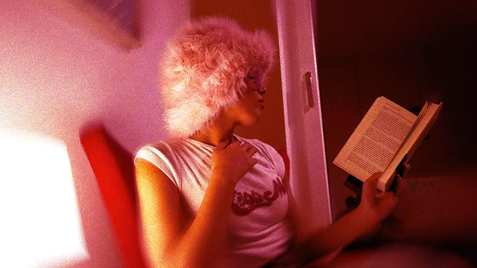 A picture of a woman in a bedroom reading a book in privacy to depict how erotica in India is consumed in hiding as well as Indian erotica consumption via smut