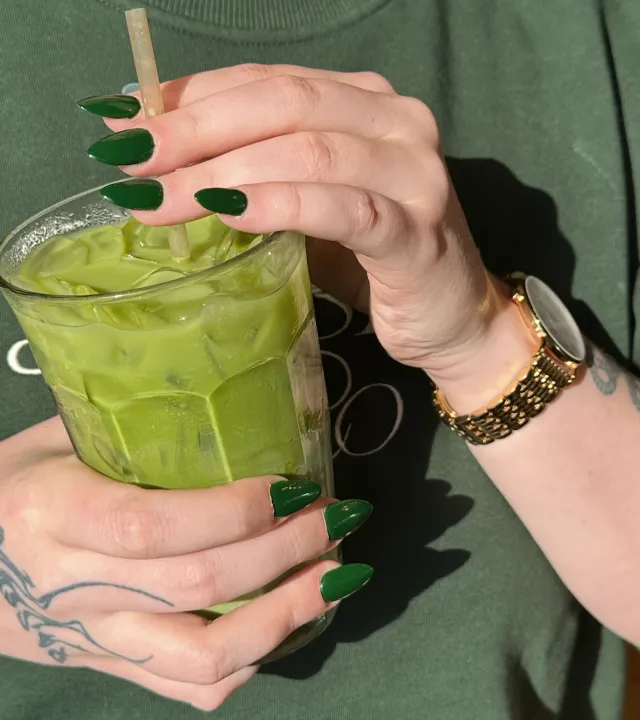 A tall glass of iced matcha latte in a woman's hand