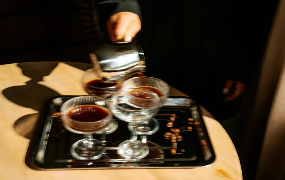 A hazy picture of a person pouring drinks into multiple glasses to show how cafe culture in India has evolved to include nightlife culture India and bar culture India with spaces that go from cafes to bar from day to night