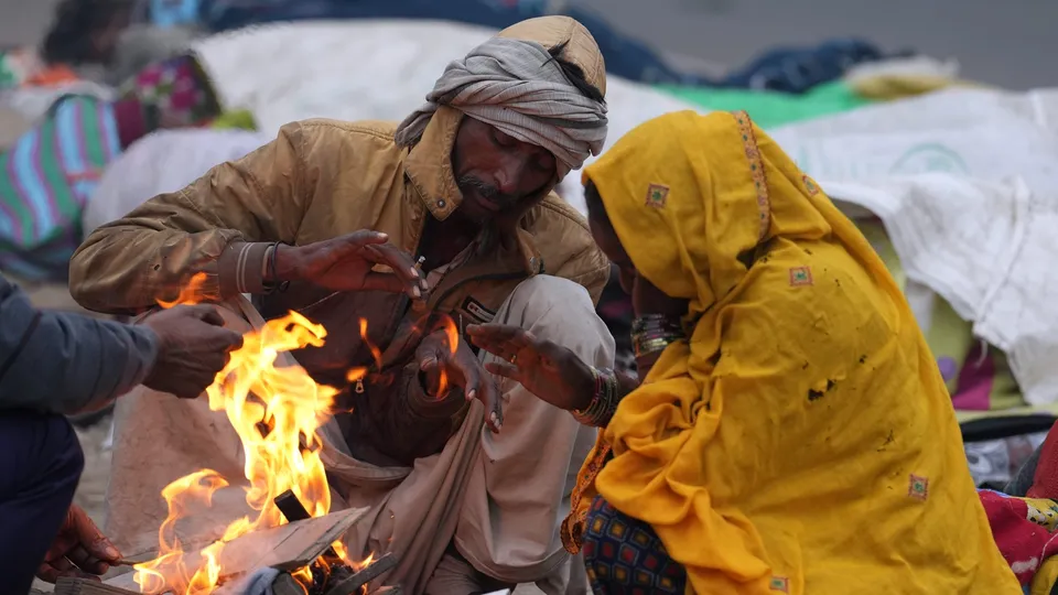 People sit around a bonfire at a roadside on a cold winter morning during fog, in New Delhi
