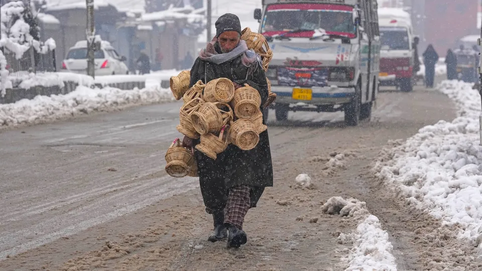 A vendor carries kangris, traditional earthen pots woven around with wicker and filled with hot embers to keep warm, after the season's first snowfall, in Srinagar, Saturday, Dec. 28, 2024