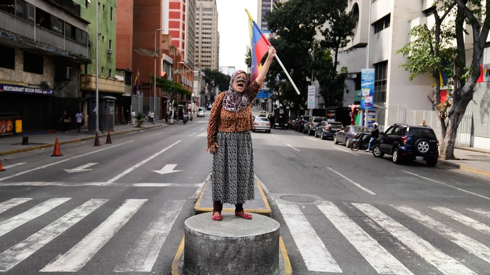 A supporter of Venezuelan President Nicolas Maduro stands on a median strip waving a national flag in Caracas, Venezuela, Saturday, Jan. 3, 2026, after U.S. President Donald Trump announced that Maduro had been captured and flown out of the country.