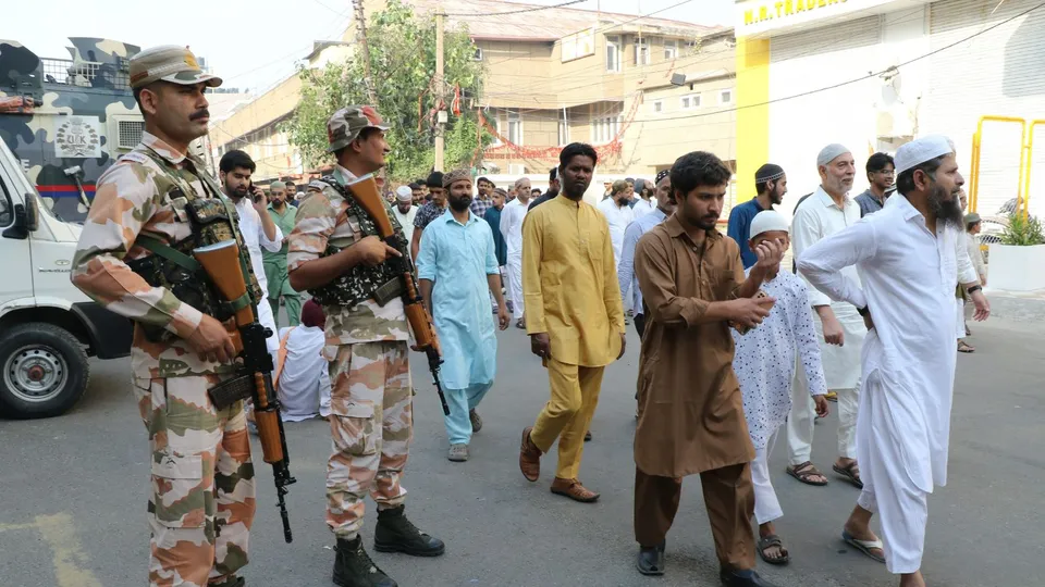 Devotees pass by security personnel standing guard during the Eid al-Adha celebration, in Jammu, Monday, June 17, 2024.