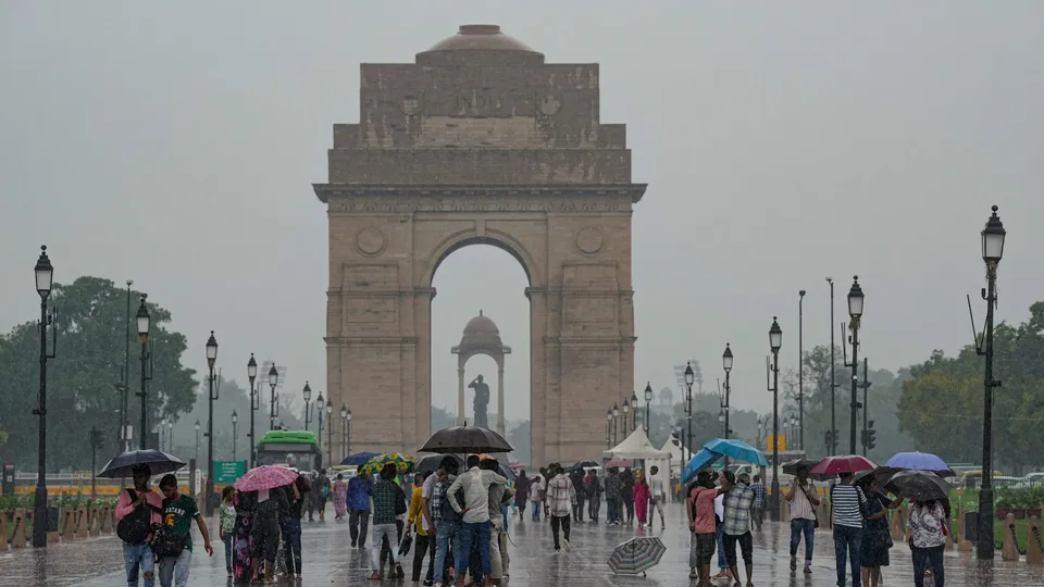 Visitors use umbrellas to shield themselves during rains at India Gate, in New Delhi