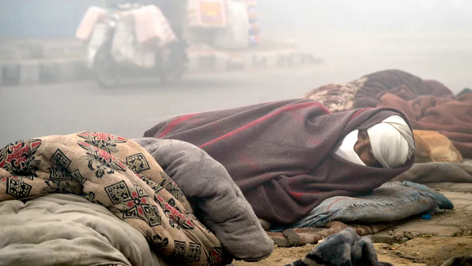A homeless man wrapped in a blanket sleeps on the pavement on a cold winter day