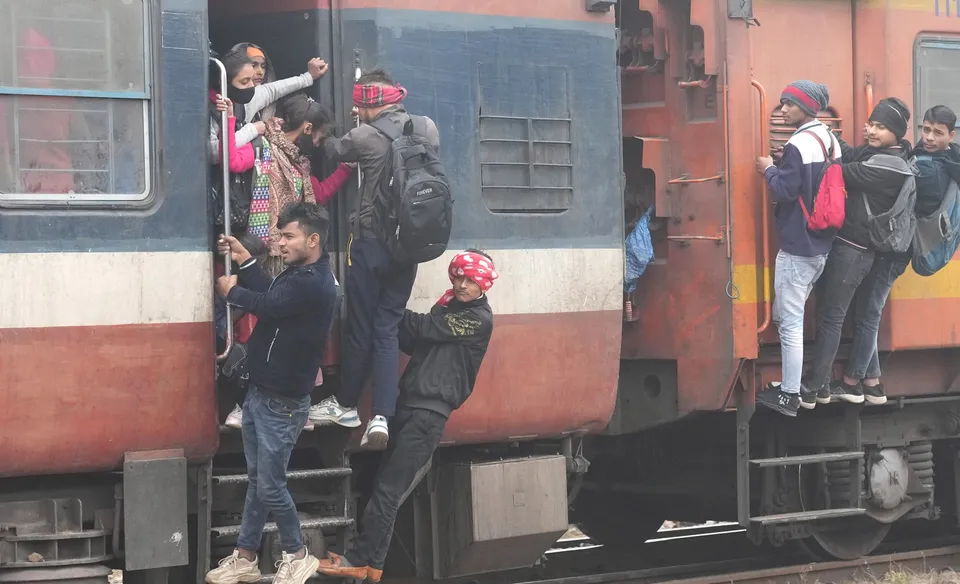 Passengers hang out from a train as it approaches a station during a cold and foggy winter morning, in New Delhi