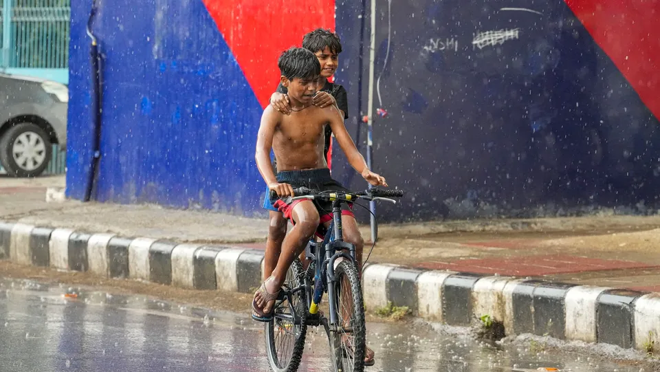 Young men ride a bicycle during rain, in New Delhi, Wednesday, May 29, 2024