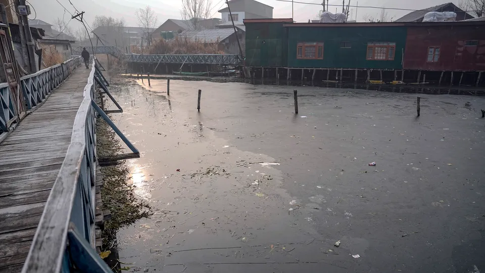 A man walks on a wooden bridge over the partially frozen interior part of Dal Lake during a cold winter morning as intense cold wave grips Kashmir valley