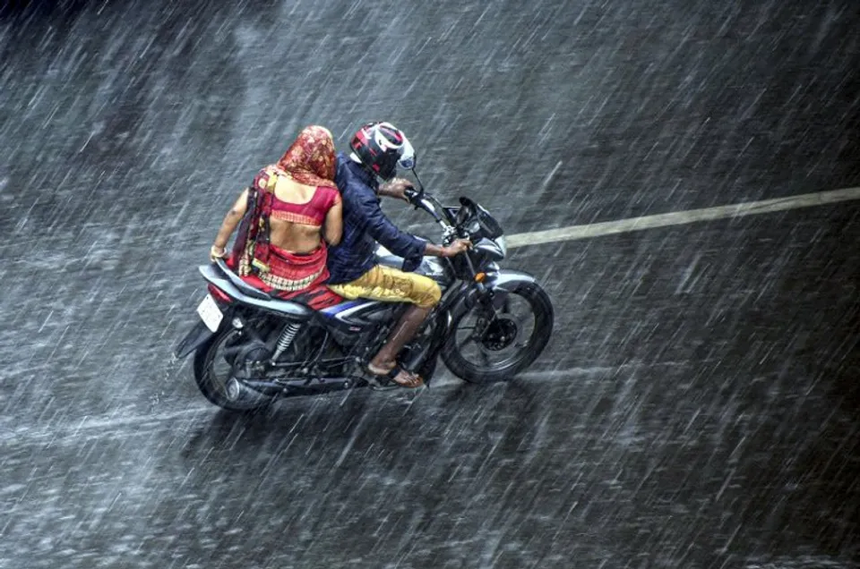 Commuters ride a bike during rain