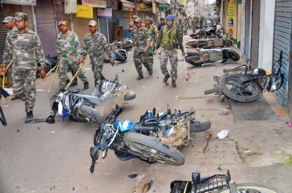 Security personnel conduct a route march as miscreants damage vehicles during a protest